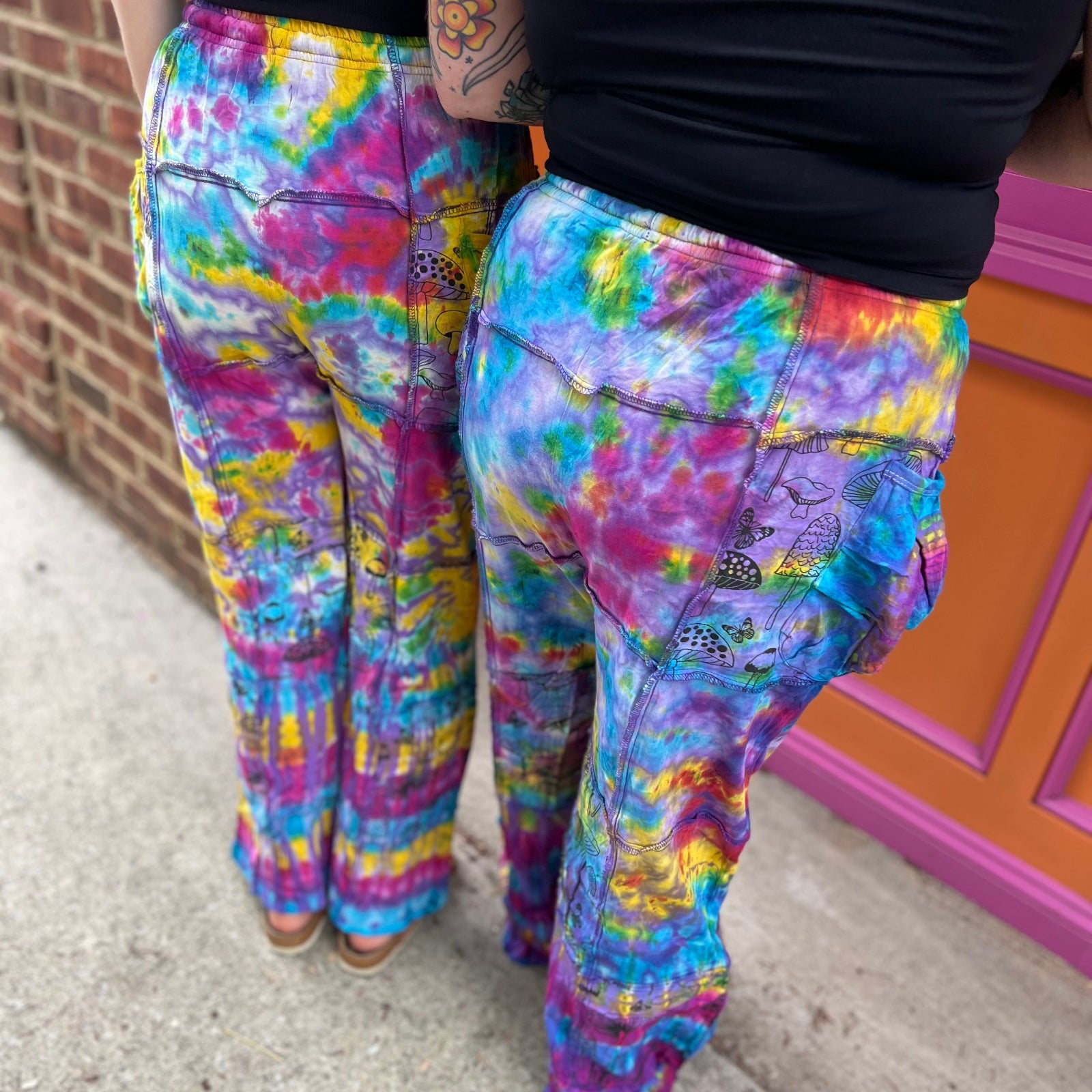 Two women wearing the Rainbow Tie Dye Pocket Bell Cotton Trousers, showing off the back.