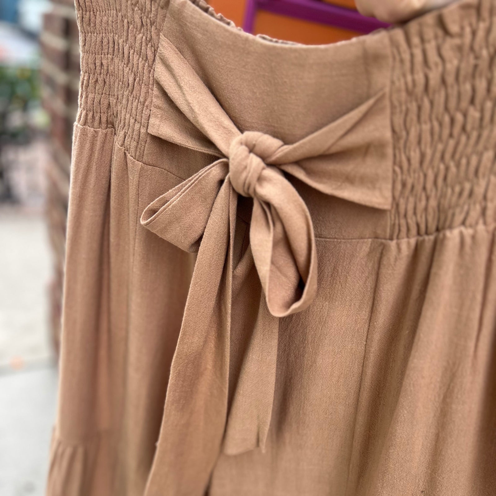 An up-close image of someone holding up the Plus Smocking Waist Tier Wide Pants in front of a brick wall.