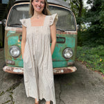 A woman wearing the oatmeal Stripe Sleeveless Ruffle Jumpsuit in front of a vintage teal Volkswagen bus.