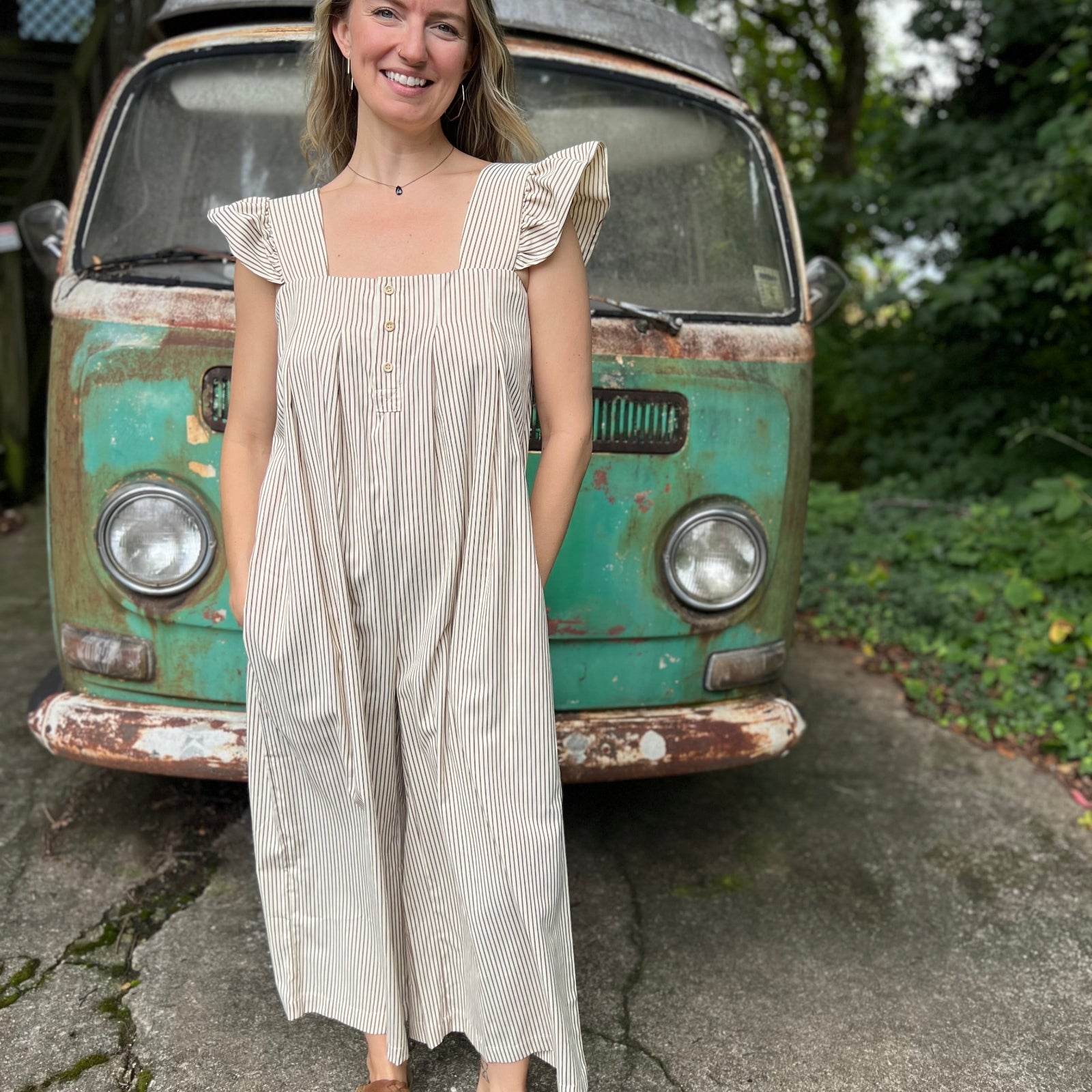 A woman wearing the oatmeal Stripe Sleeveless Ruffle Jumpsuit in front of a vintage teal Volkswagen bus.