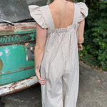 A woman wearing the oatmeal Stripe Sleeveless Ruffle Jumpsuit in front of a vintage teal Volkswagen bus.