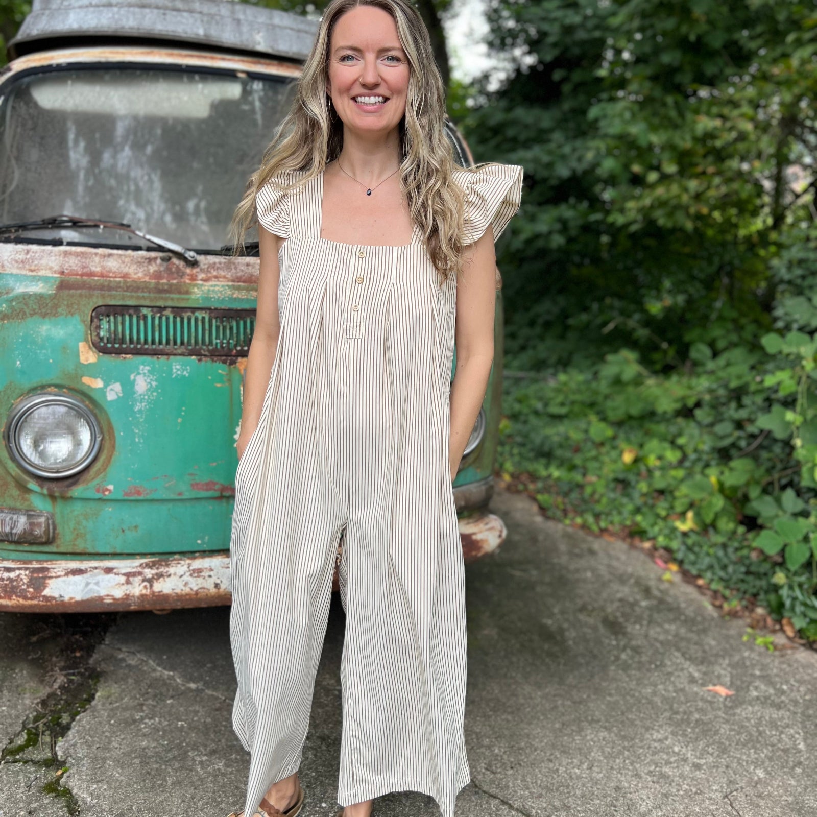 A woman wearing the oatmeal Stripe Sleeveless Ruffle Jumpsuit in front of a vintage teal Volkswagen bus.
