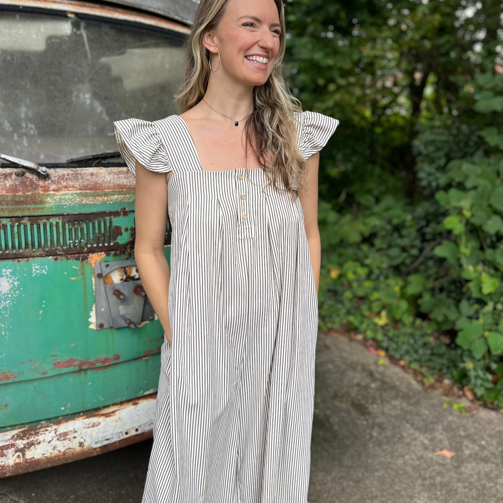 A woman wearing the black Stripe Sleeveless Ruffle Jumpsuit in front of a vintage teal Volkswagen bus.