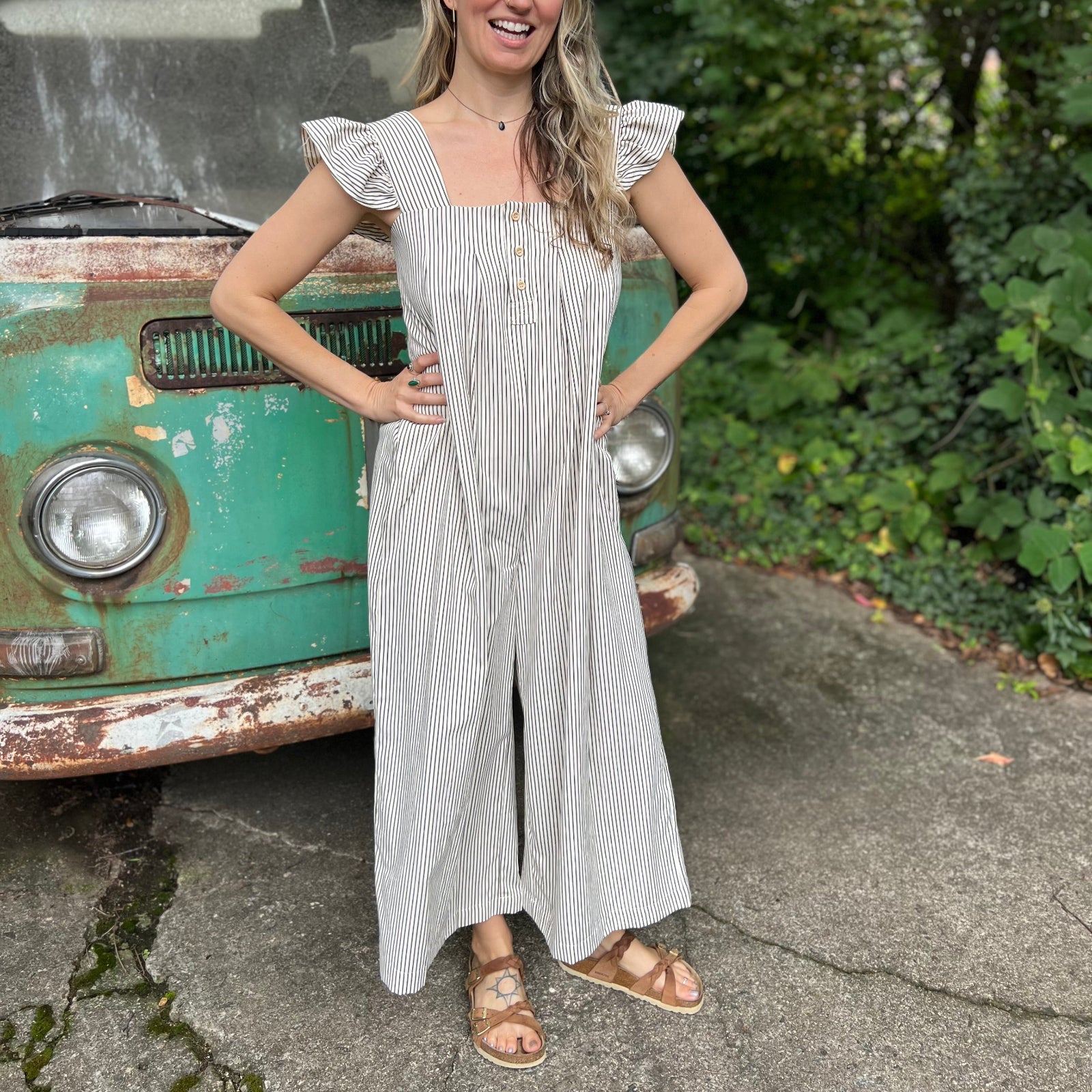 A woman wearing the black Stripe Sleeveless Ruffle Jumpsuit in front of a vintage teal Volkswagen bus.