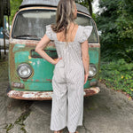 A woman wearing the black Stripe Sleeveless Ruffle Jumpsuit in front of a vintage teal Volkswagen bus.