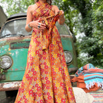 Woman in a colorful dress standing in front of a vintage van with greenery in the background