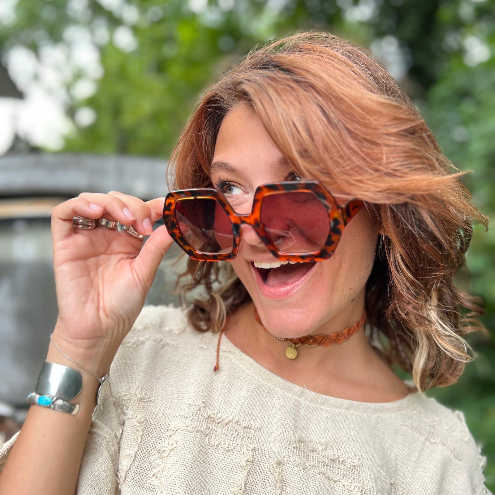 A woman wearing the tortoise Iris Seventies Hexagon Sunglasses with a cream top.