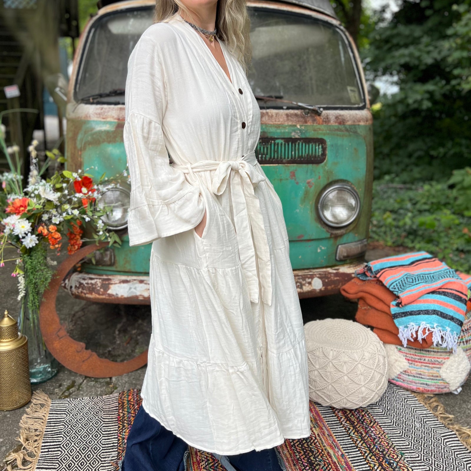 A woman wearing the white Organic Tiered Maxi Kimono Wrap Dress in front of a vintage Volkswagen bus.