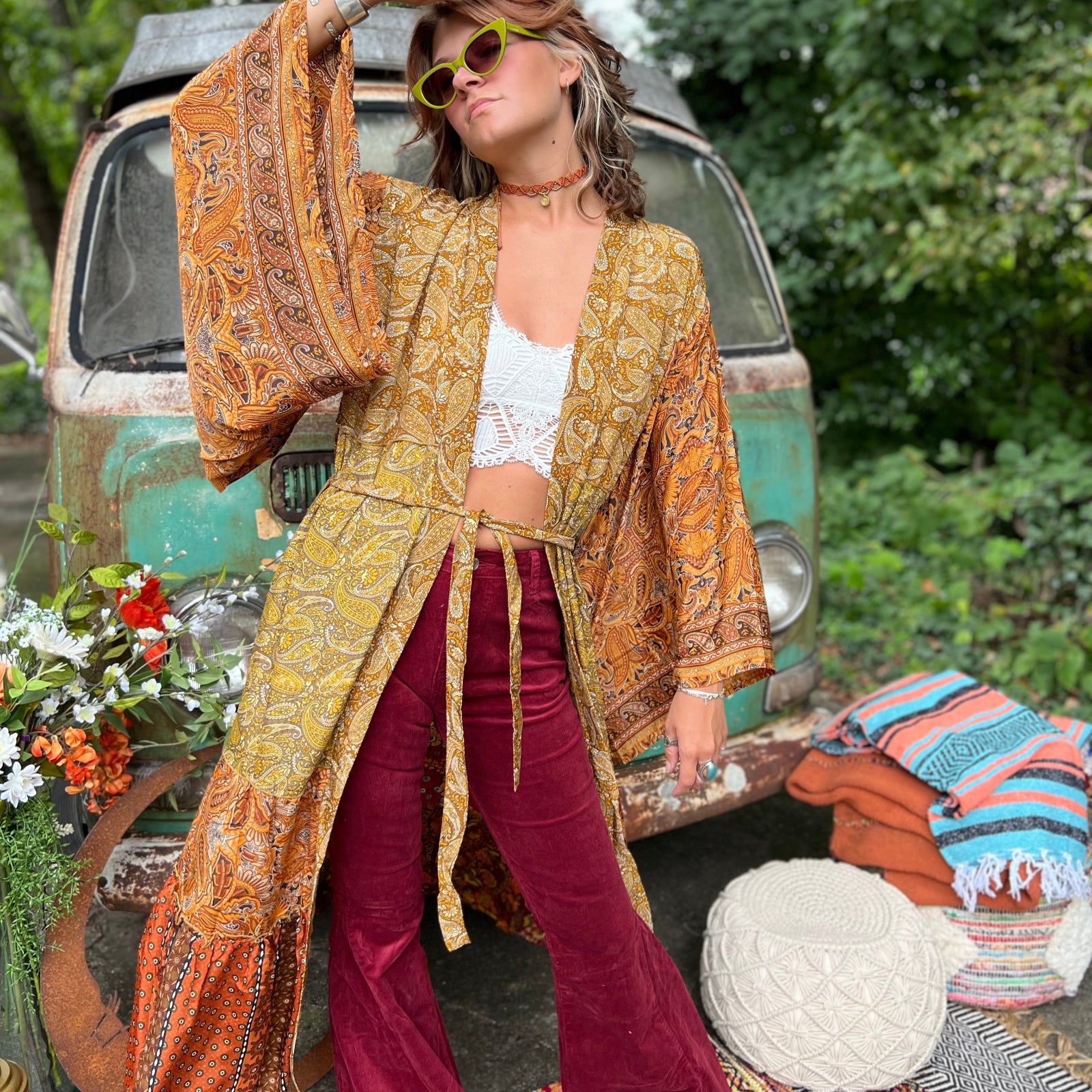 A woman the Hippie Golden Patchwork Kimono Robe Duster with a white bralette and red velvet bellbottoms in front of a vintage Volkswagen bus.