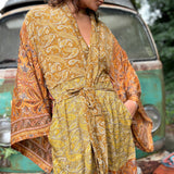 A woman the Hippie Golden Patchwork Kimono Robe Duster with a white bralette and red velvet bellbottoms in front of a vintage Volkswagen bus.