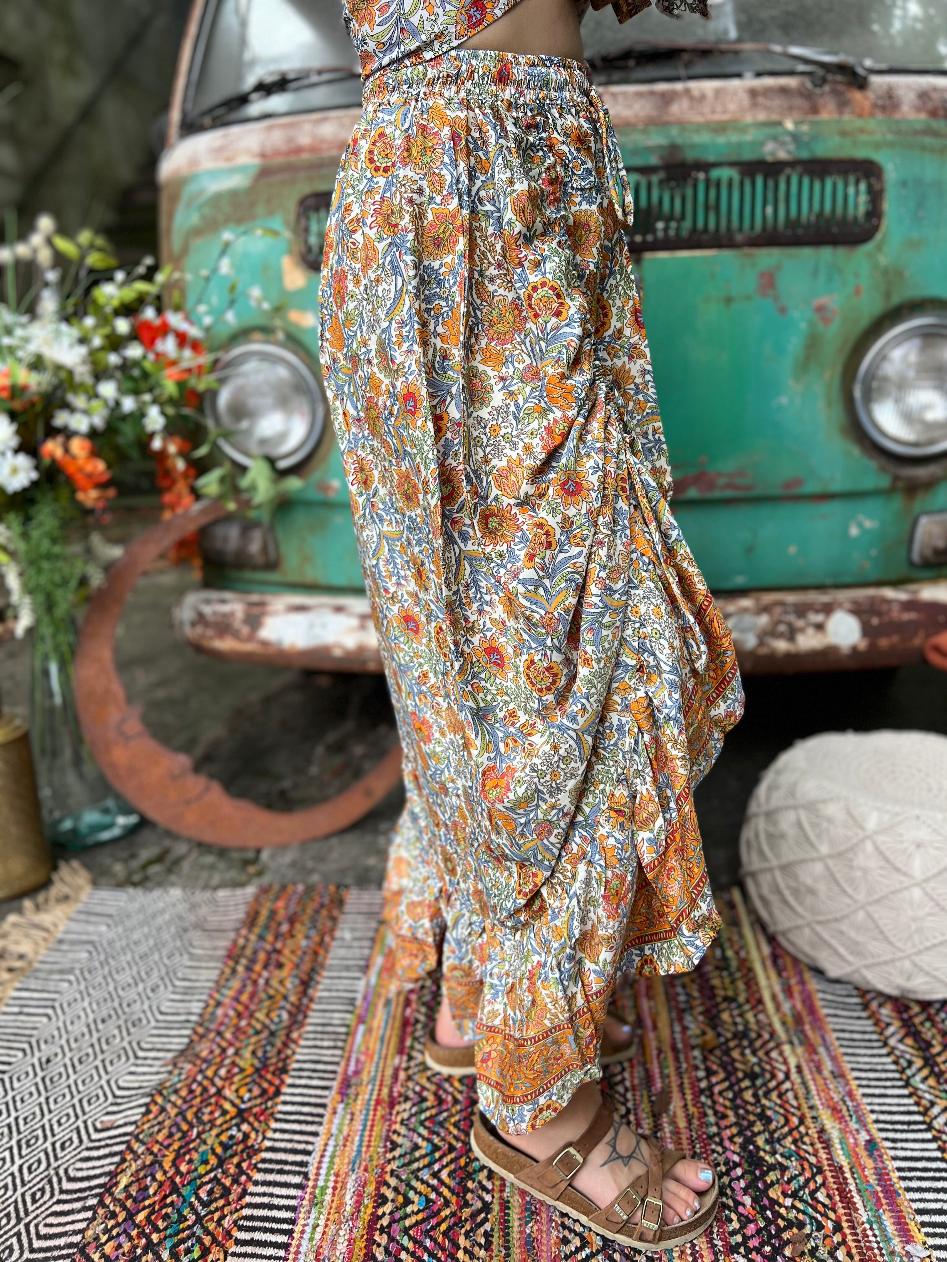Someone wearing the orange & cream Hippie Floral Cinch Maxi Ruffle Skirt in front of a Volkswagen bus.