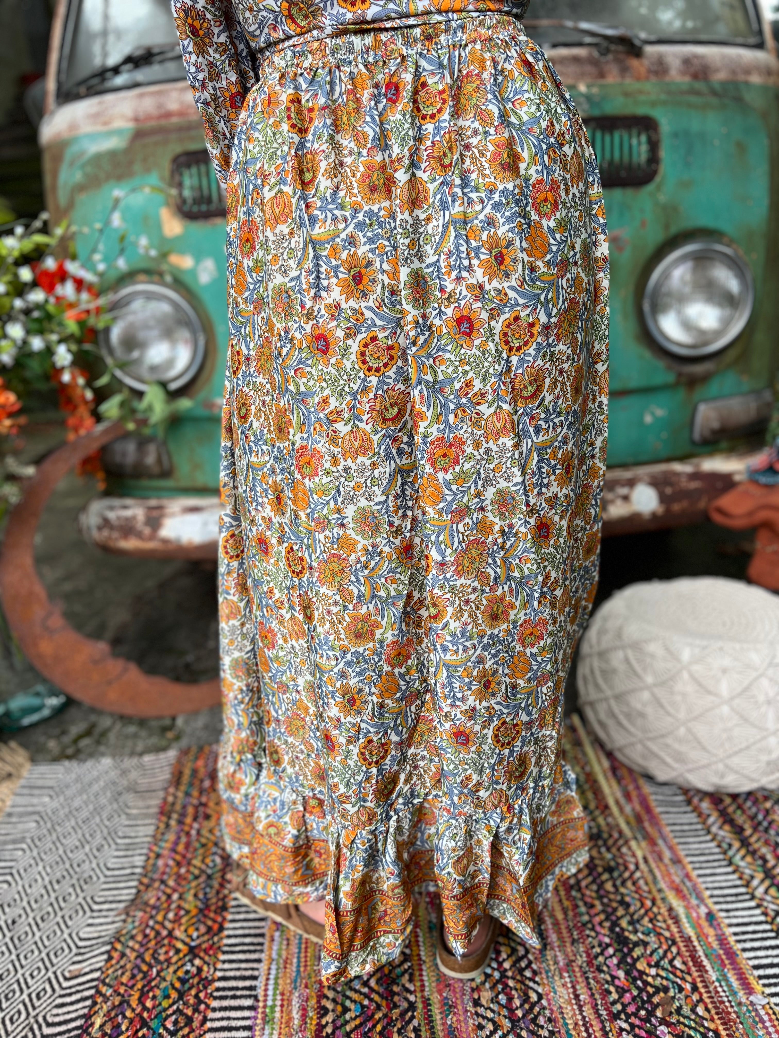Someone wearing the orange & cream Hippie Floral Cinch Maxi Ruffle Skirt in front of a Volkswagen bus.