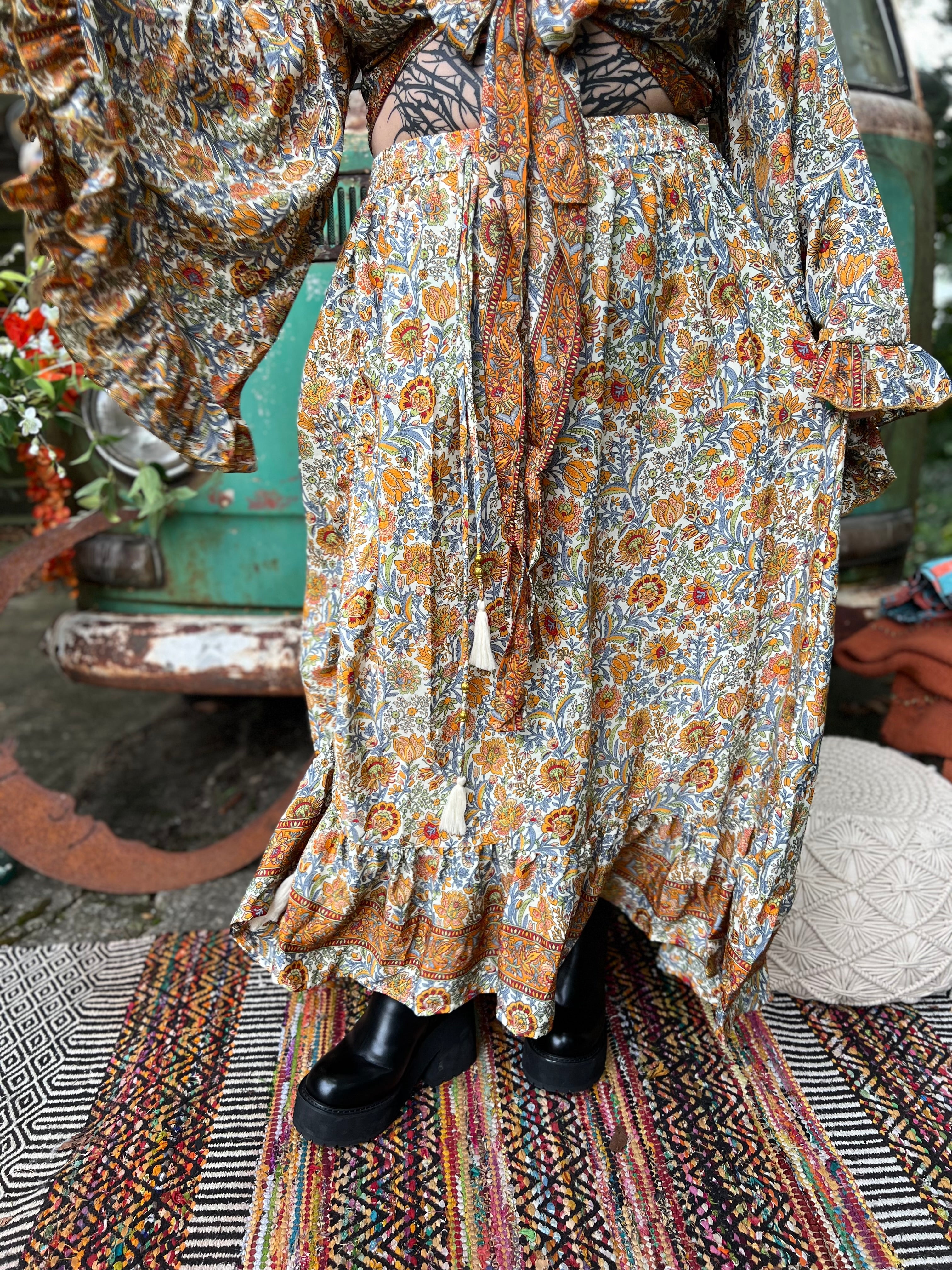Someone wearing the orange & cream Hippie Floral Cinch Maxi Ruffle Skirt in front of a Volkswagen bus.