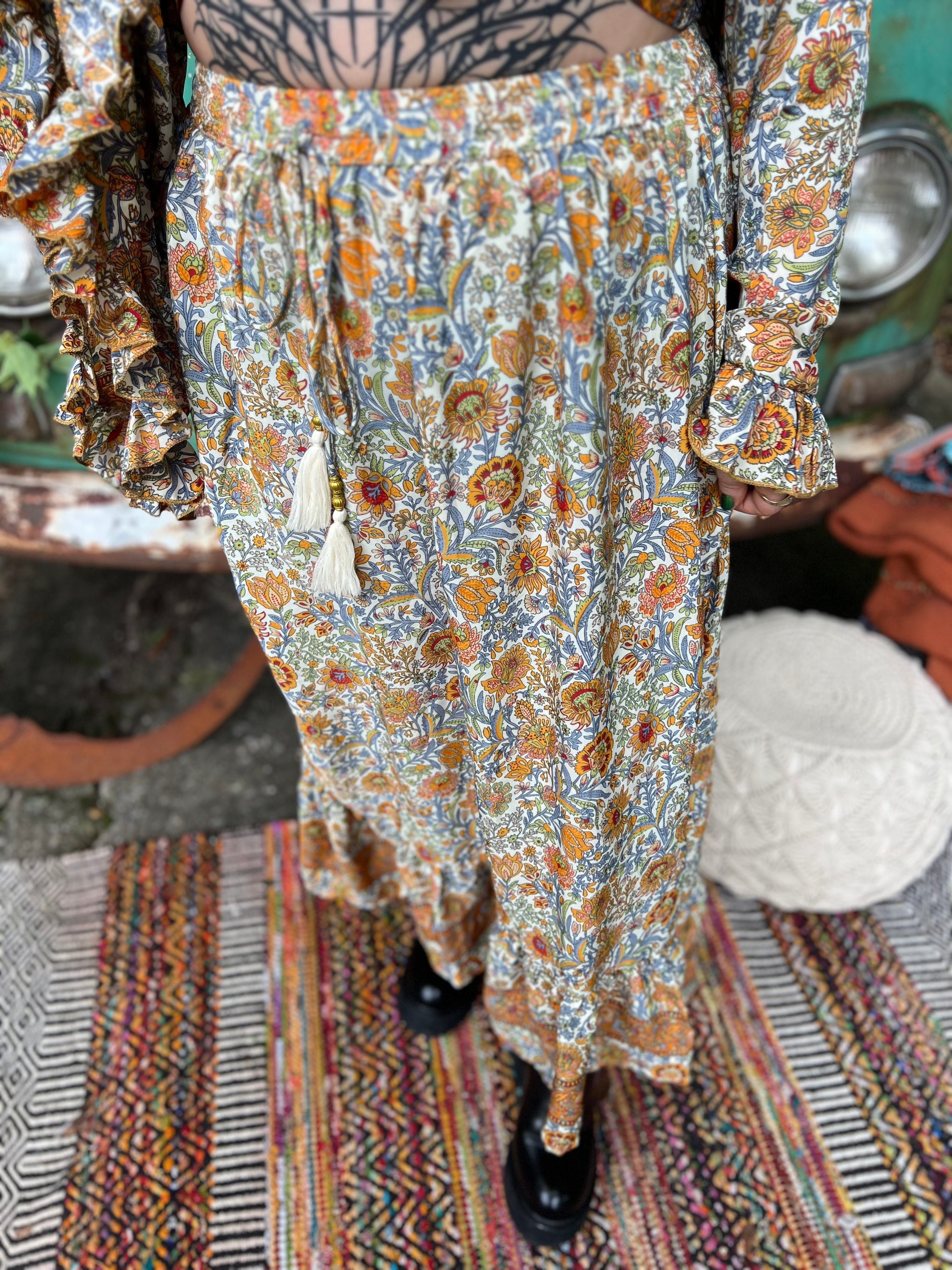 Someone wearing the orange & cream Hippie Floral Cinch Maxi Ruffle Skirt in front of a Volkswagen bus.