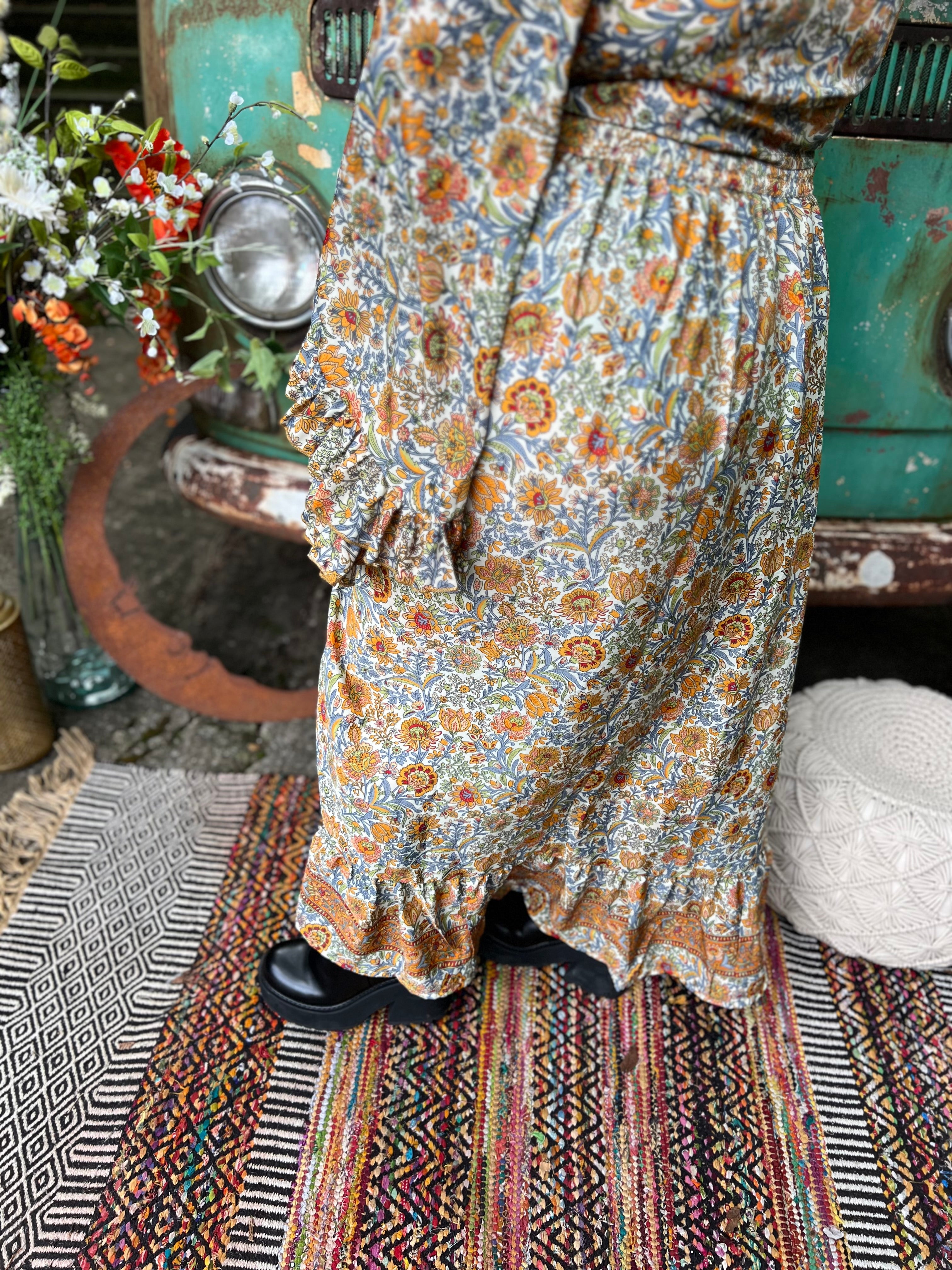 Someone wearing the orange & cream Hippie Floral Cinch Maxi Ruffle Skirt in front of a Volkswagen bus.