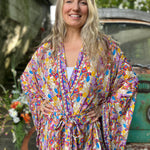 A woman wearing the Rainbow Hippie Boho Psychedelic Kimono Robe in front of a vintage Volkswagen bus.