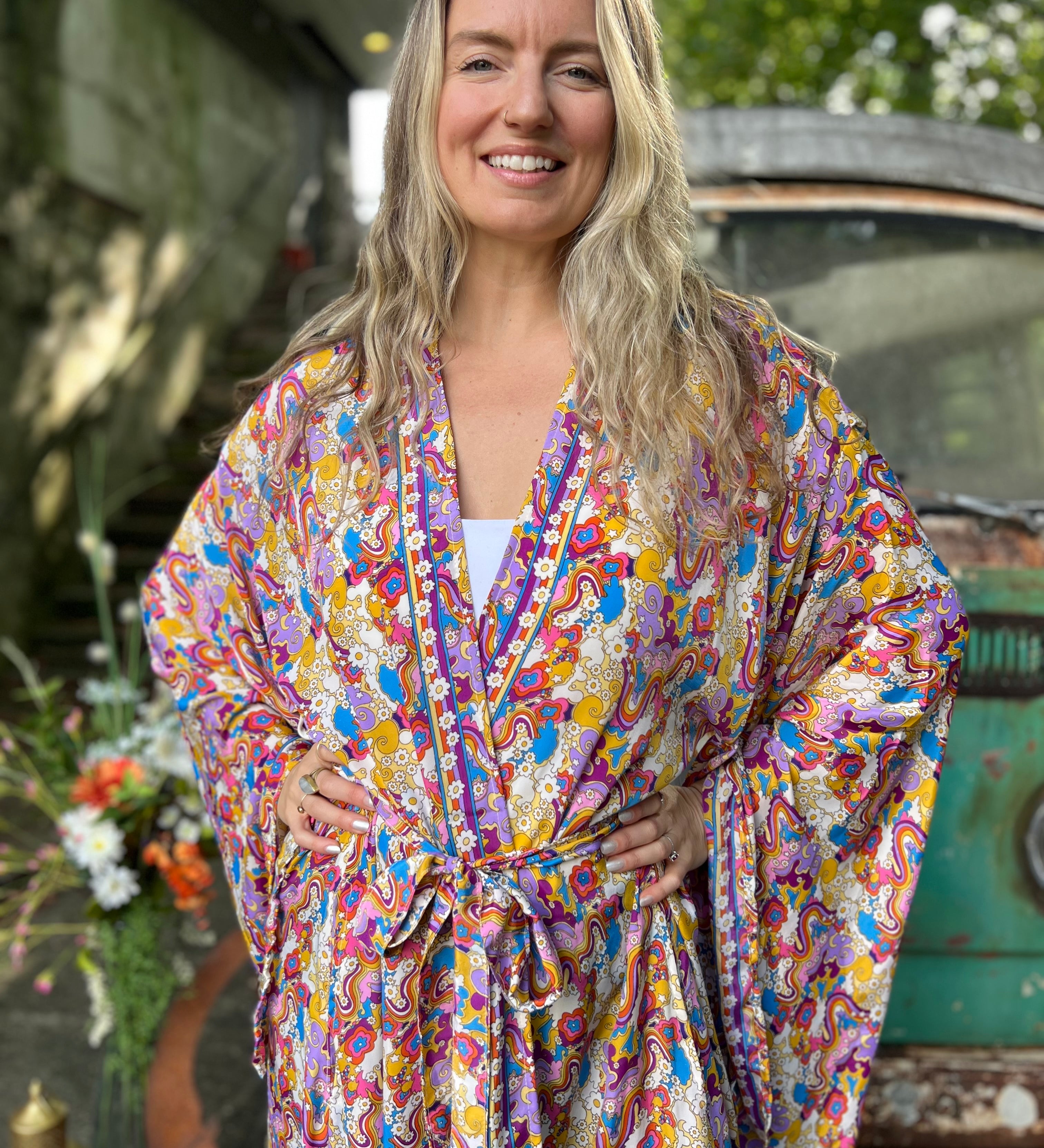 A woman wearing the Rainbow Hippie Boho Psychedelic Kimono Robe in front of a vintage Volkswagen bus.