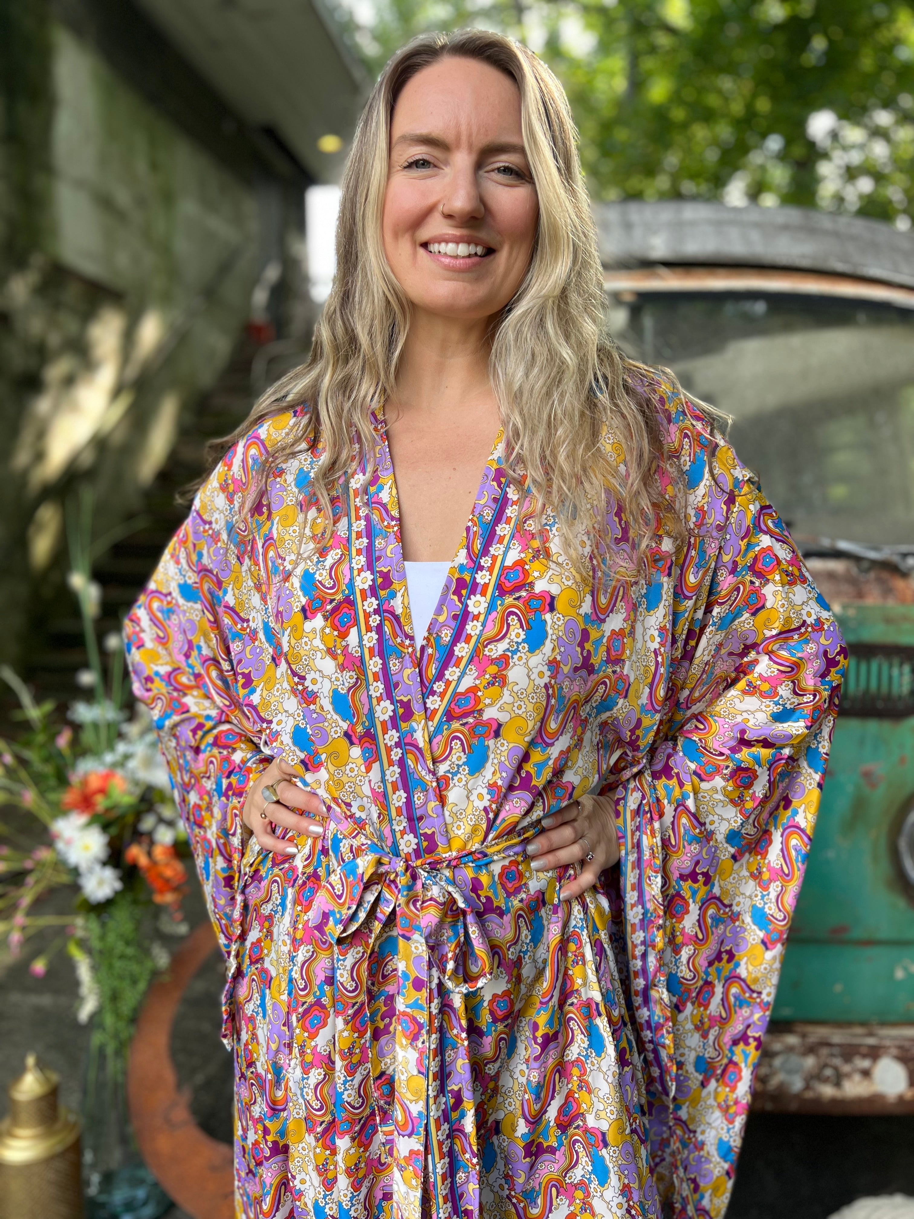 A woman wearing the Rainbow Hippie Boho Psychedelic Kimono Robe in front of a vintage Volkswagen bus.