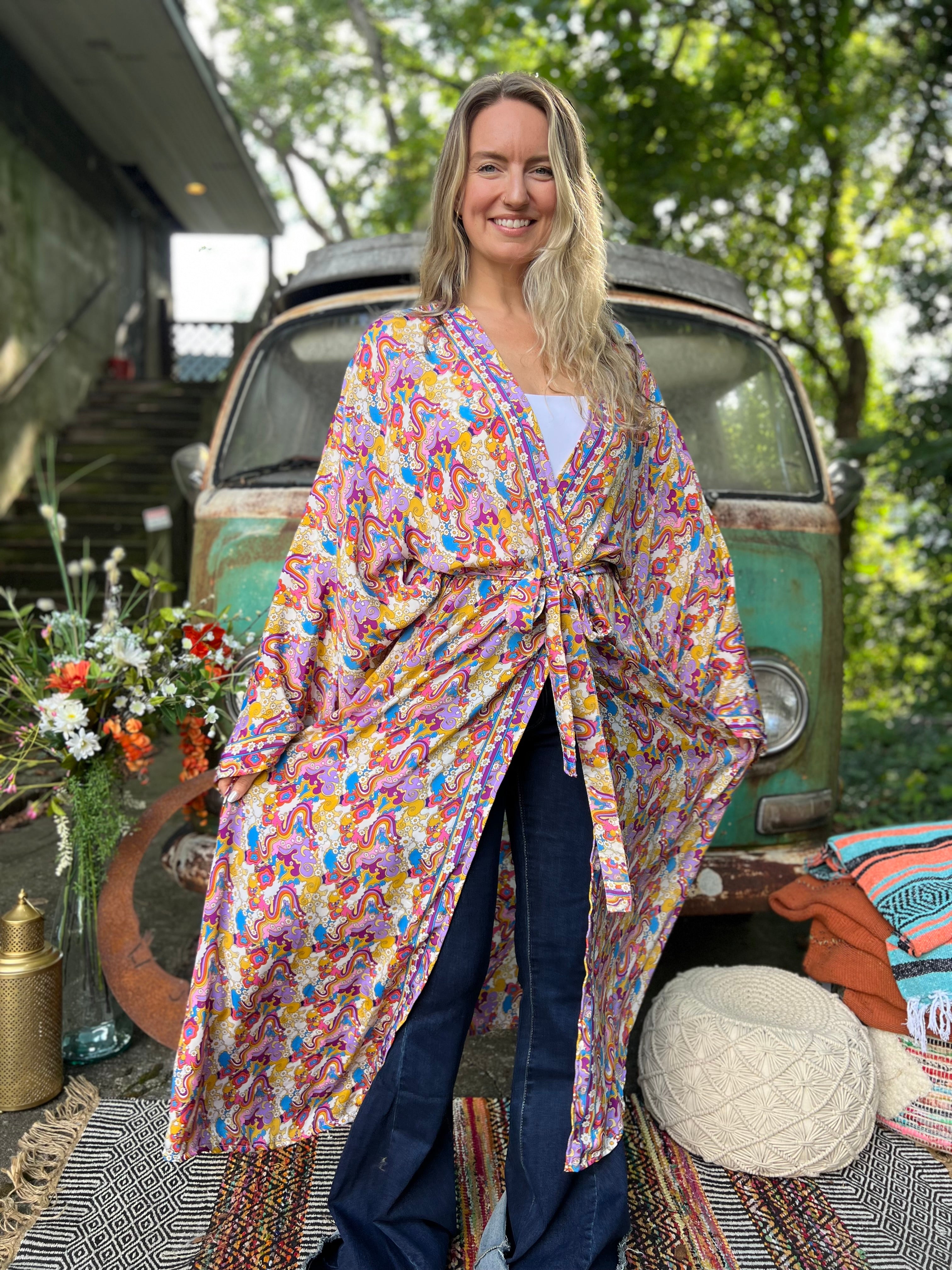 A woman wearing the Rainbow Hippie Boho Psychedelic Kimono Robe in front of a vintage Volkswagen bus.