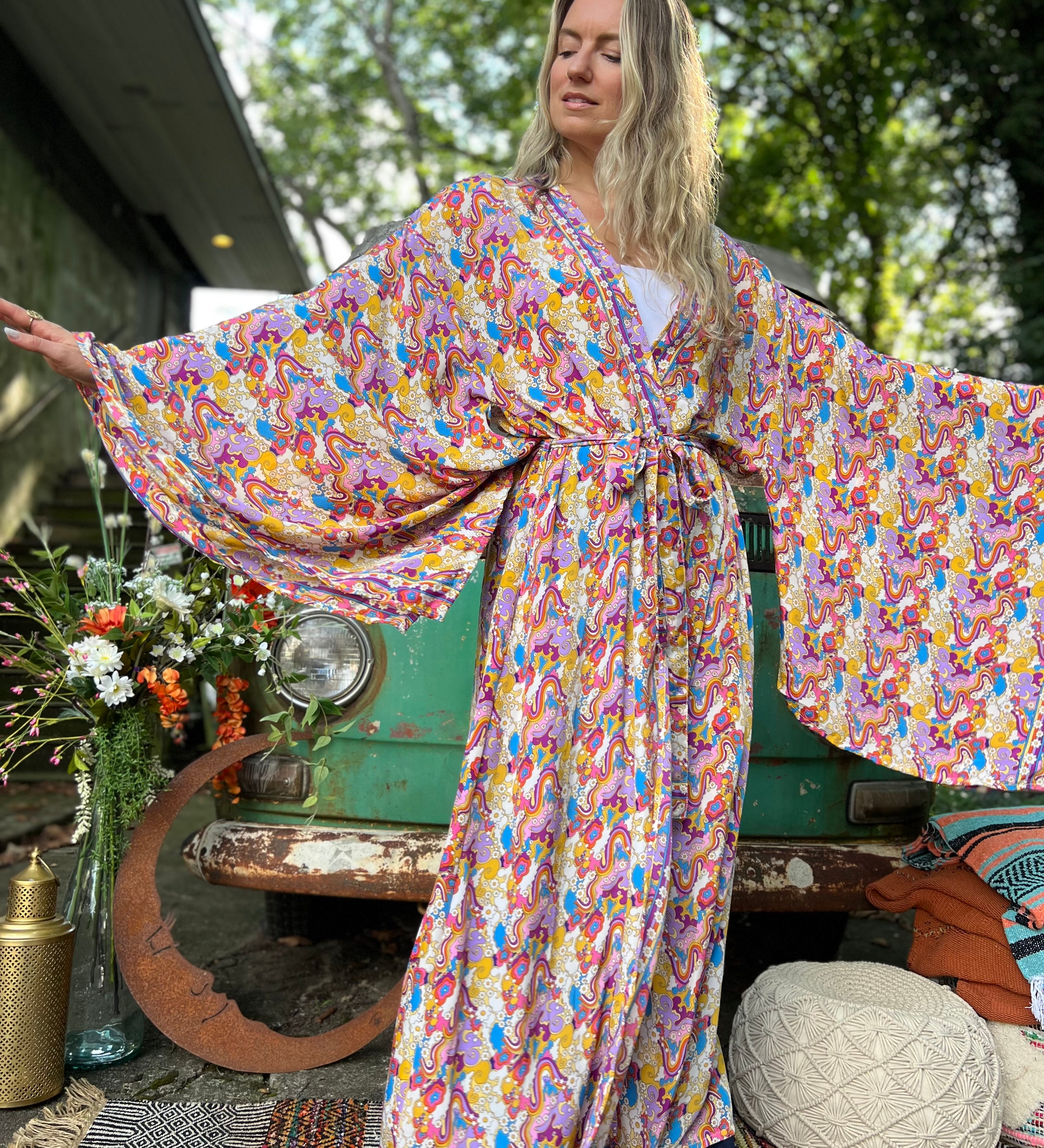 A woman wearing the Rainbow Hippie Boho Psychedelic Kimono Robe in front of a vintage Volkswagen bus.