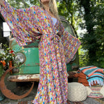 A woman wearing the Rainbow Hippie Boho Psychedelic Kimono Robe in front of a vintage Volkswagen bus.