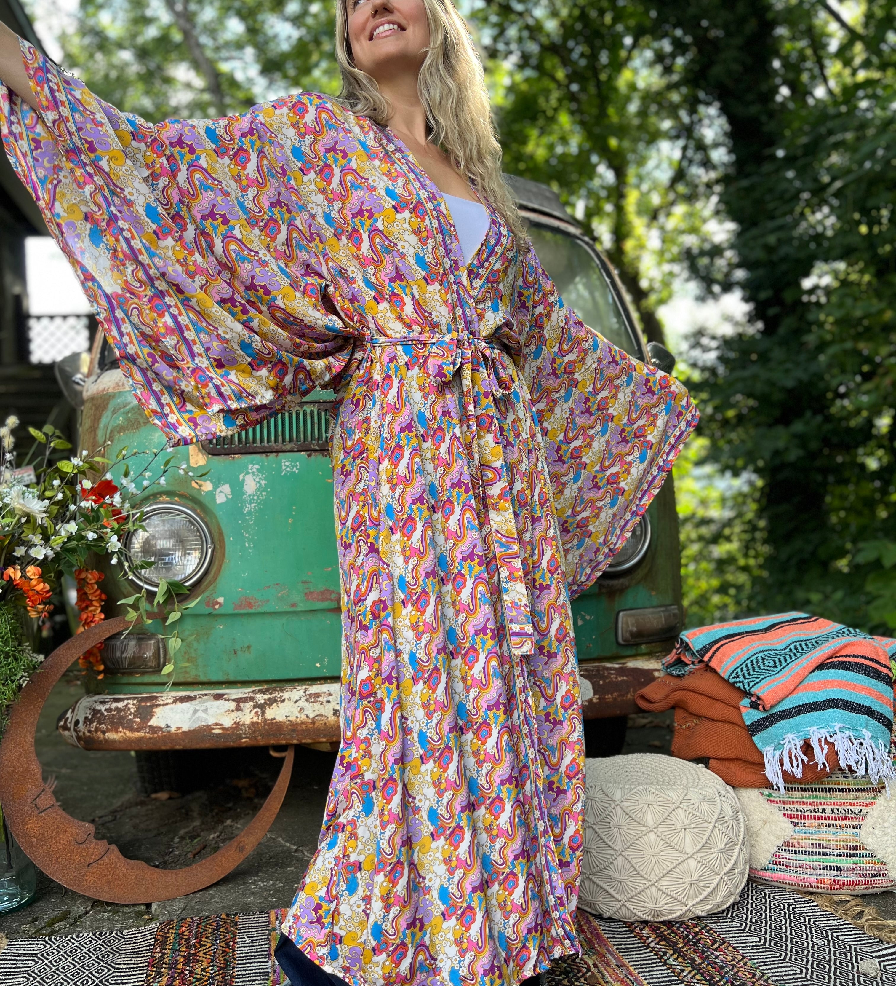 A woman wearing the Rainbow Hippie Boho Psychedelic Kimono Robe in front of a vintage Volkswagen bus.