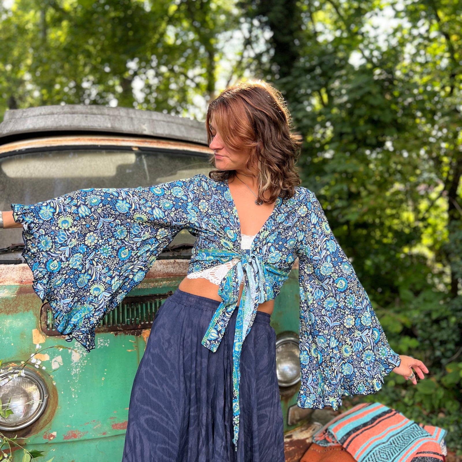 A woman wearing the blue Hippie Bohemian Bell Sleeve Wrap Top with black pants in front of a rusted vintage Volkswagen bus.