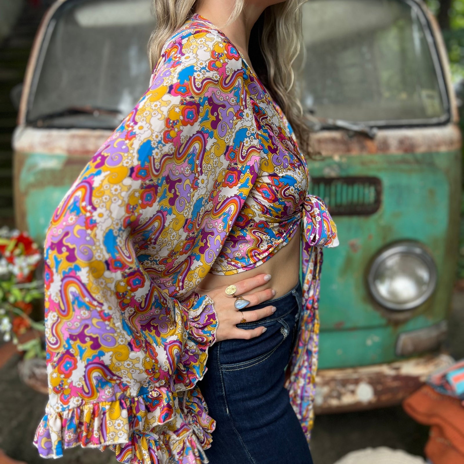 A woman wearing the rainbow Hippie Bohemian Bell Sleeve Wrap Top with black pants in front of a rusted vintage Volkswagen bus.