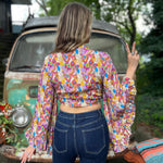 A woman wearing the rainbow Hippie Bohemian Bell Sleeve Wrap Top with black pants in front of a rusted vintage Volkswagen bus.