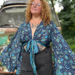 A woman wearing the blue Hippie Bohemian Bell Sleeve Wrap Top with black pants in front of a rusted vintage Volkswagen bus.