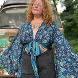 A woman wearing the blue Hippie Bohemian Bell Sleeve Wrap Top with black pants in front of a rusted vintage Volkswagen bus.
