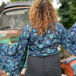A woman wearing the blue Hippie Bohemian Bell Sleeve Wrap Top with black pants in front of a rusted vintage Volkswagen bus.