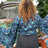 A woman wearing the blue Hippie Bohemian Bell Sleeve Wrap Top with black pants in front of a rusted vintage Volkswagen bus.