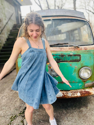 carefree vibes denim mini dress twirling in front of an old VW bus