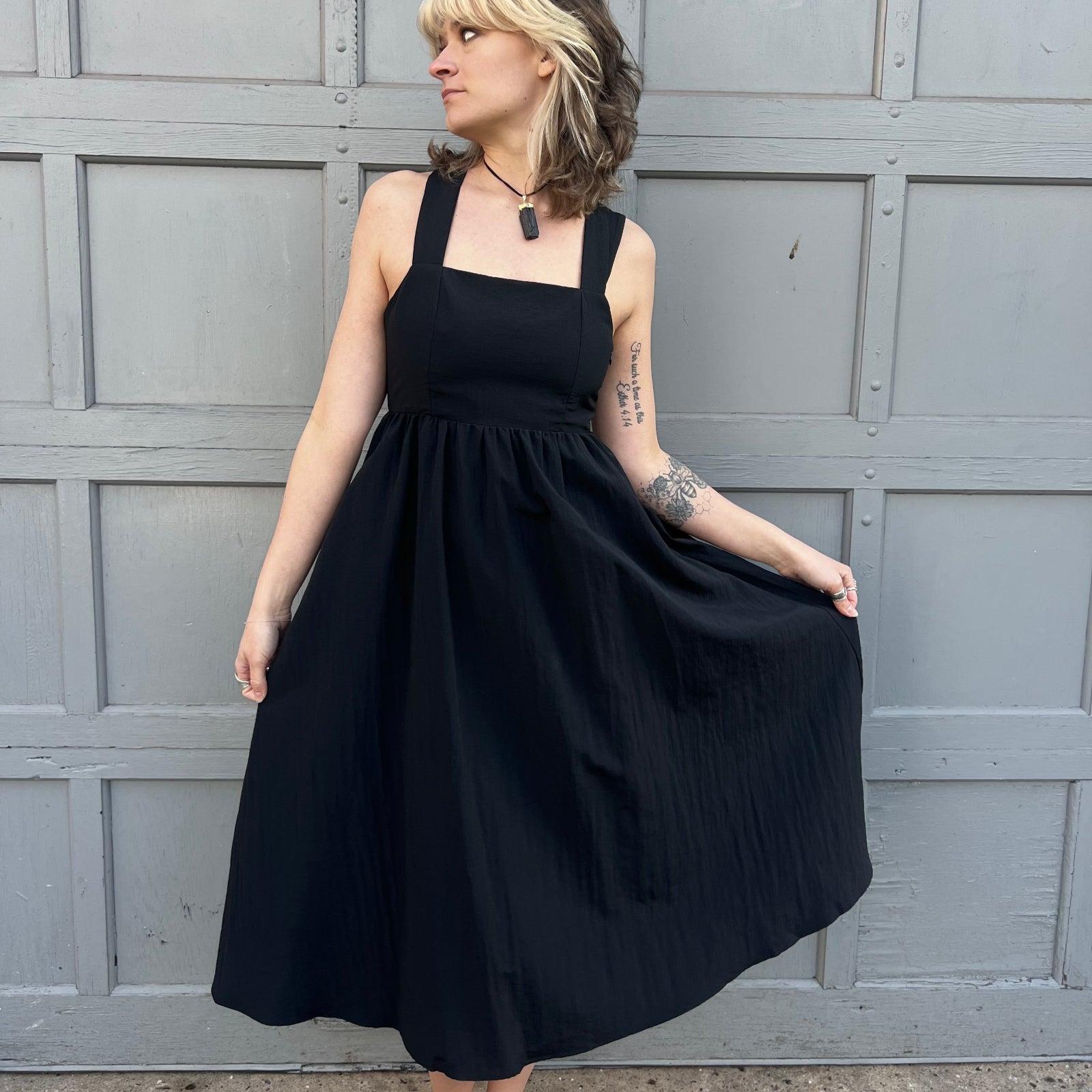 A woman wearing the Black Woven Polyester Nylon Back Cross Strap Midi Dress with sandals and a black crystal necklace.