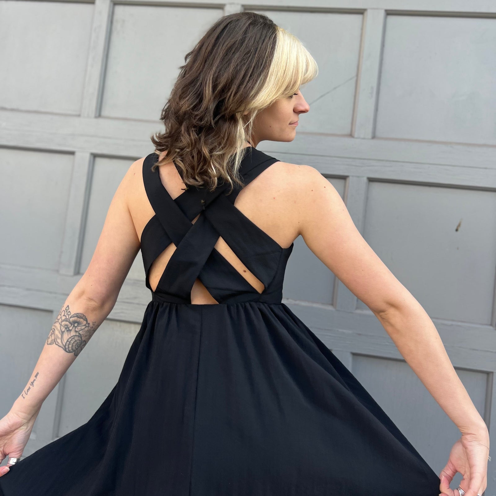 A woman wearing the Black Woven Polyester Nylon Back Cross Strap Midi Dress with sandals and a black crystal necklace, showing off the crossover back.