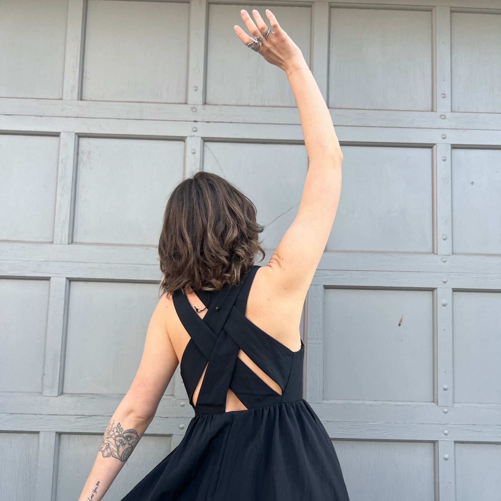 A woman wearing the Black Woven Polyester Nylon Back Cross Strap Midi Dress with sandals and a black crystal necklace, showing off the crossover back.