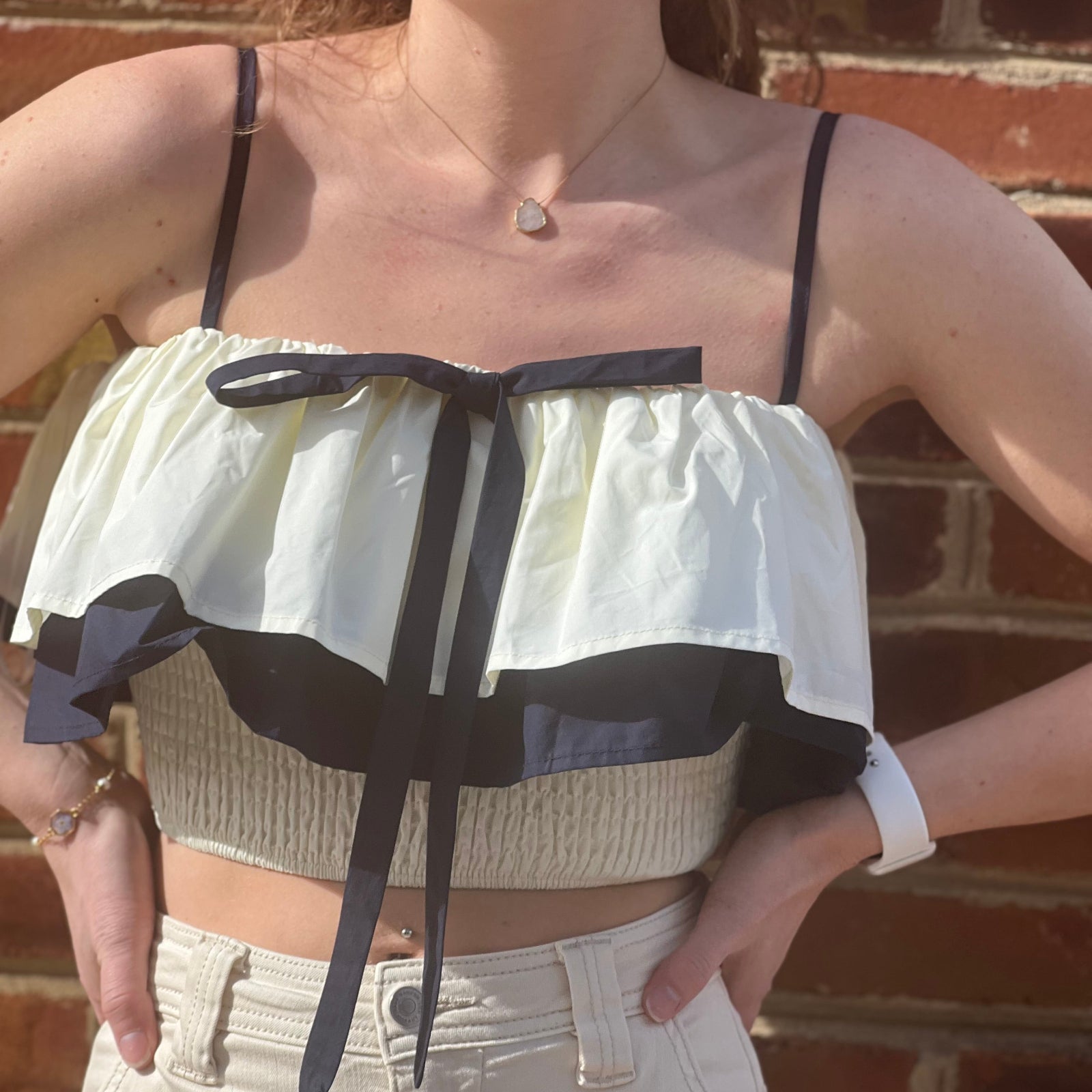 A woman wearing the Contrast Cotton Flare Bow Top with white jeans in front of a brick wall.
