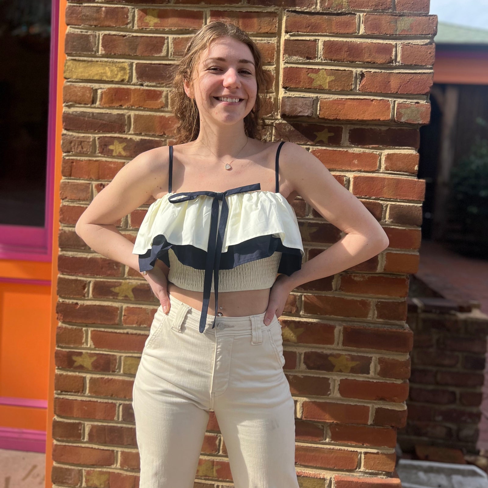 A woman wearing the Contrast Cotton Flare Bow Top with white jeans in front of a brick wall.