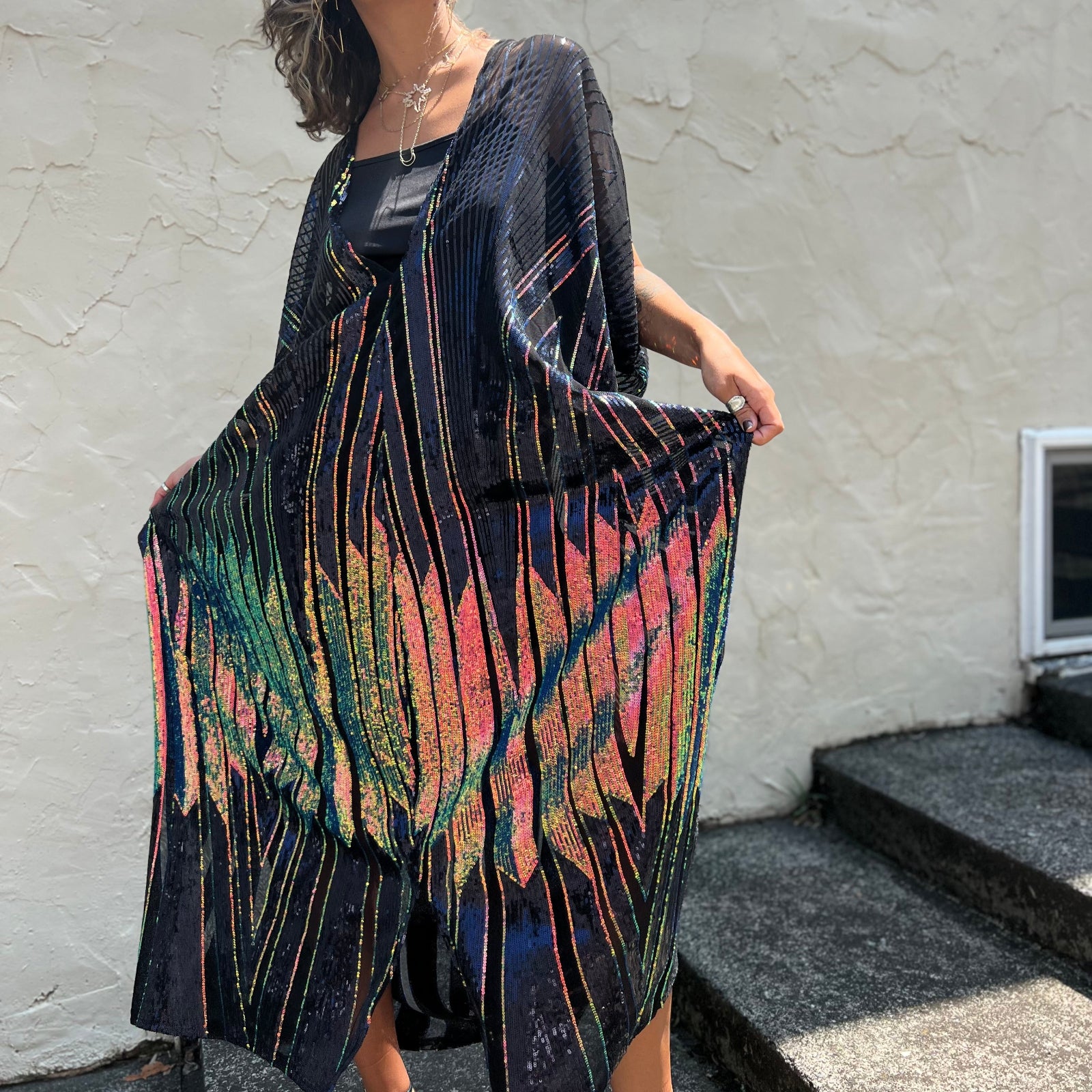 A woman wearing the Midnight Lotus Caftan with a black dress and heels.