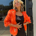 A woman wearing the Planet Queen Orange Faux Fur Jacket with a black dress in front of a window.