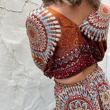 A woman wearing the orange Woven Floral Paisley Top and Trouser Set in font of a white wall.