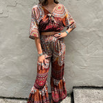 A woman wearing the orange Woven Floral Paisley Top and Trouser Set in font of a white wall.