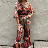 A woman wearing the orange Woven Floral Paisley Top and Trouser Set in font of a white wall.