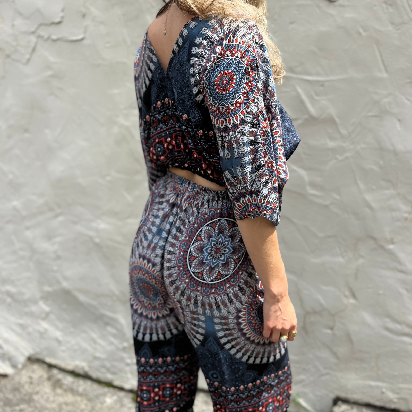 A woman wearing the blue Woven Floral Paisley Top and Trouser Set in front of a white wall.
