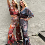Two women wearing the orange and blue Woven Floral Paisley Top and Trouser Set in front of a white wall.