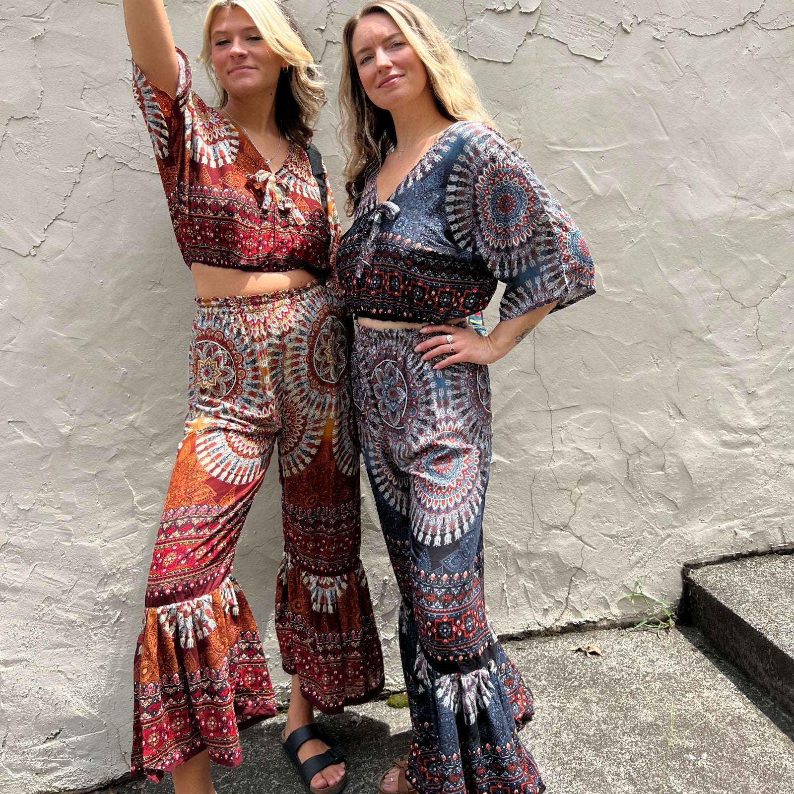 Two women wearing the orange and blue Woven Floral Paisley Top and Trouser Set in front of a white wall.
