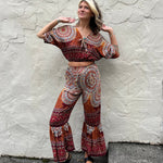 A woman wearing the orange Woven Floral Paisley Top and Trouser Set in font of a white wall.