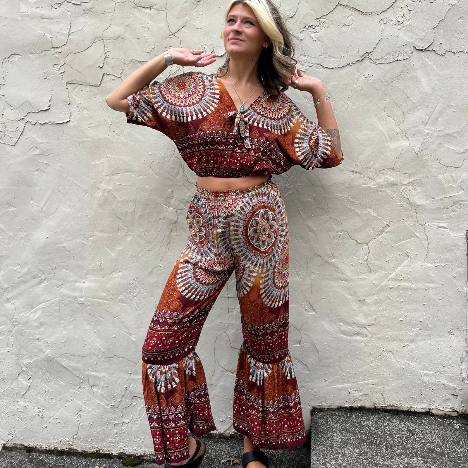 A woman wearing the orange Woven Floral Paisley Top and Trouser Set in font of a white wall.