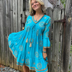 A woman wearing the Cotton Crepe Lace Embroidery Turquoise Dress in front of a wooden fence.